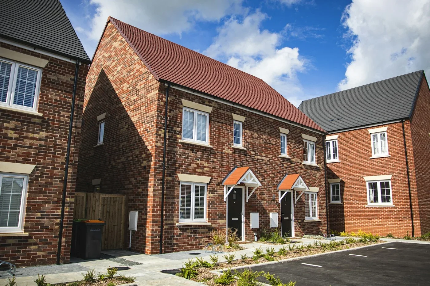 A row of modest brick new-build houses with front doors and planted borders